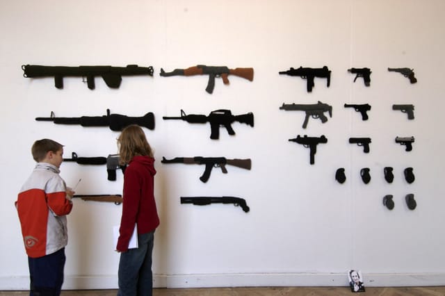 “Weapons”, 2007, assorted crocheted weapons, including hand guns and other military equipment, Wool, polyester filler and flower sticks, copyright Hanne G.