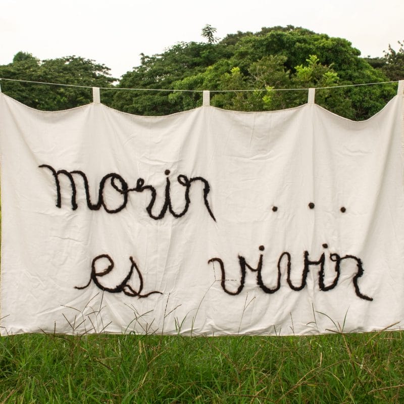 Series: This Earth Is My Whole Body. To die... is to live. 2021. Tanka. Fragment of the National Anthem of Cuba. Hand embroidery (Inlay of hair with black thread on white cotton fabric, sewn in antiseptic fabric). Human hair, cotton fabric, antiseptic fabric and yarn. 200 x 120 cm